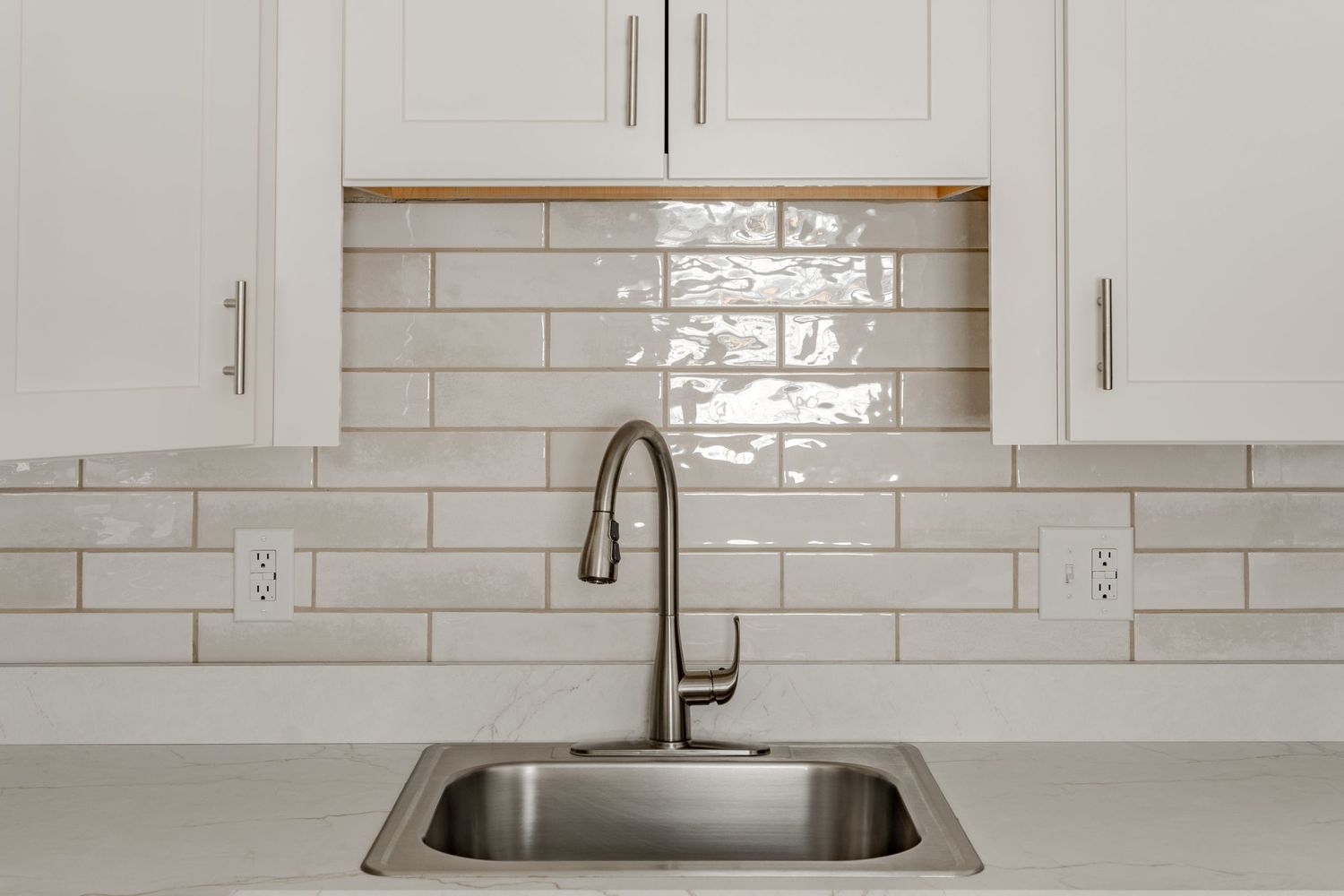 Close-up of a kitchen backsplash with subway tile, stainless sink and gooseneck faucet
