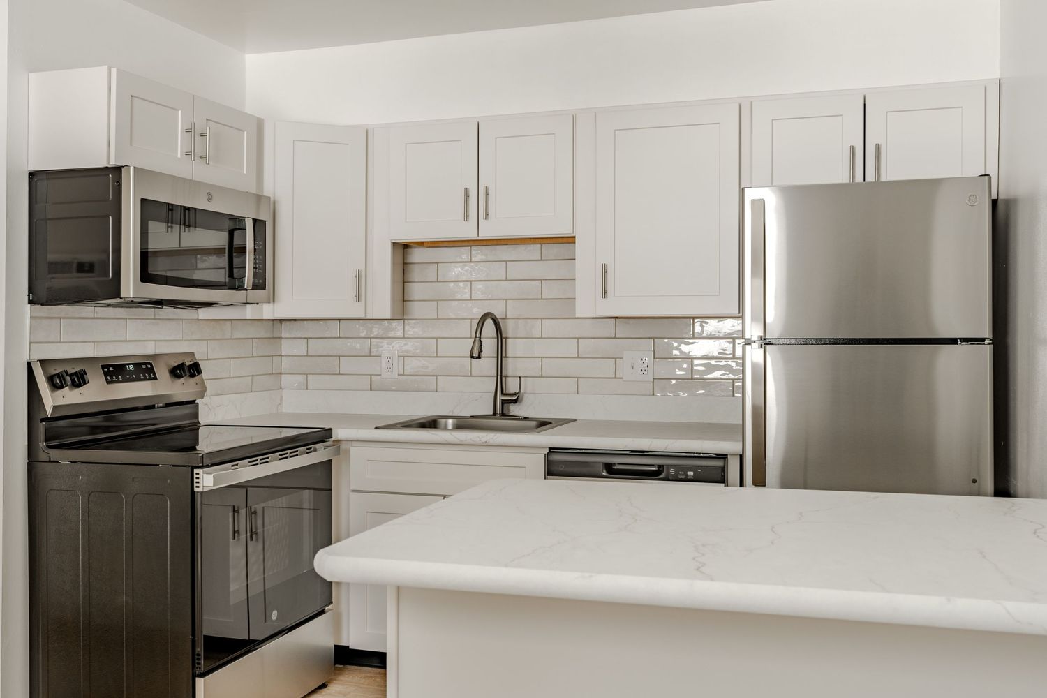 L-shaped kitchen with white cabinets, stainless appliances and a subway tile backsplash