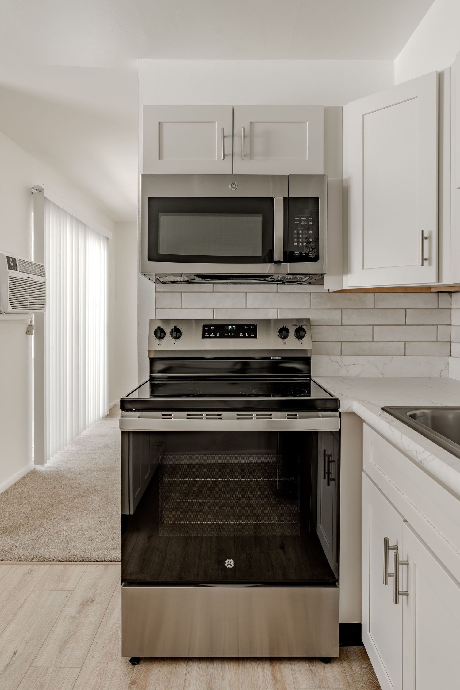 Kitchen with white cabinets, stainless stove and microwave, and subway tile backsplash