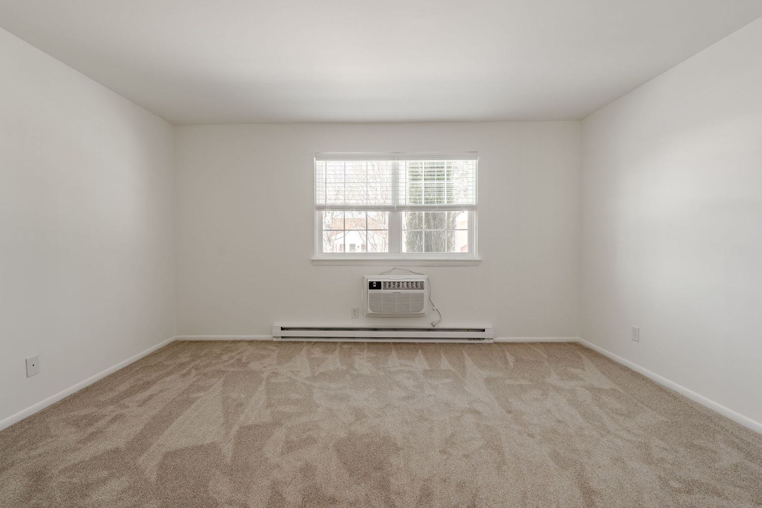 Empty carpeted bedroom with a large window and a wall-mounted air conditioner