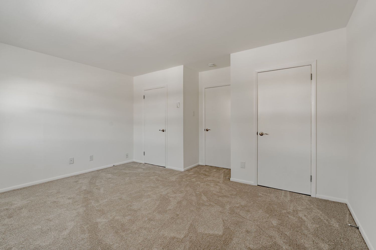 Empty carpeted room with three white closet doors