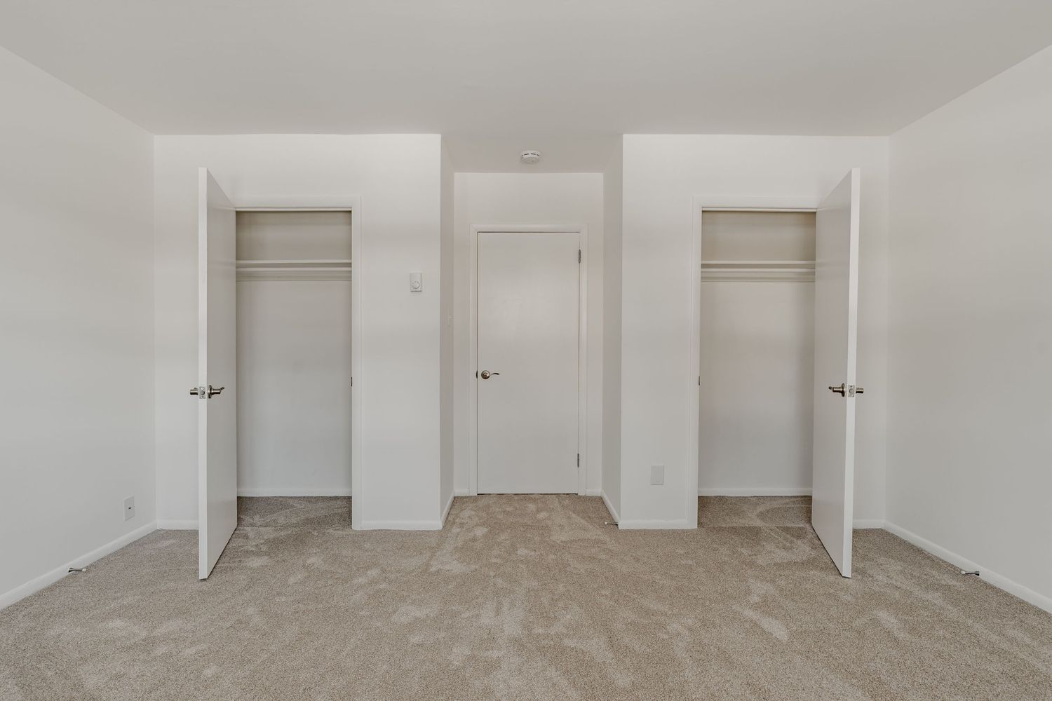 Empty carpeted room with two open reach-in closets flanking a center door