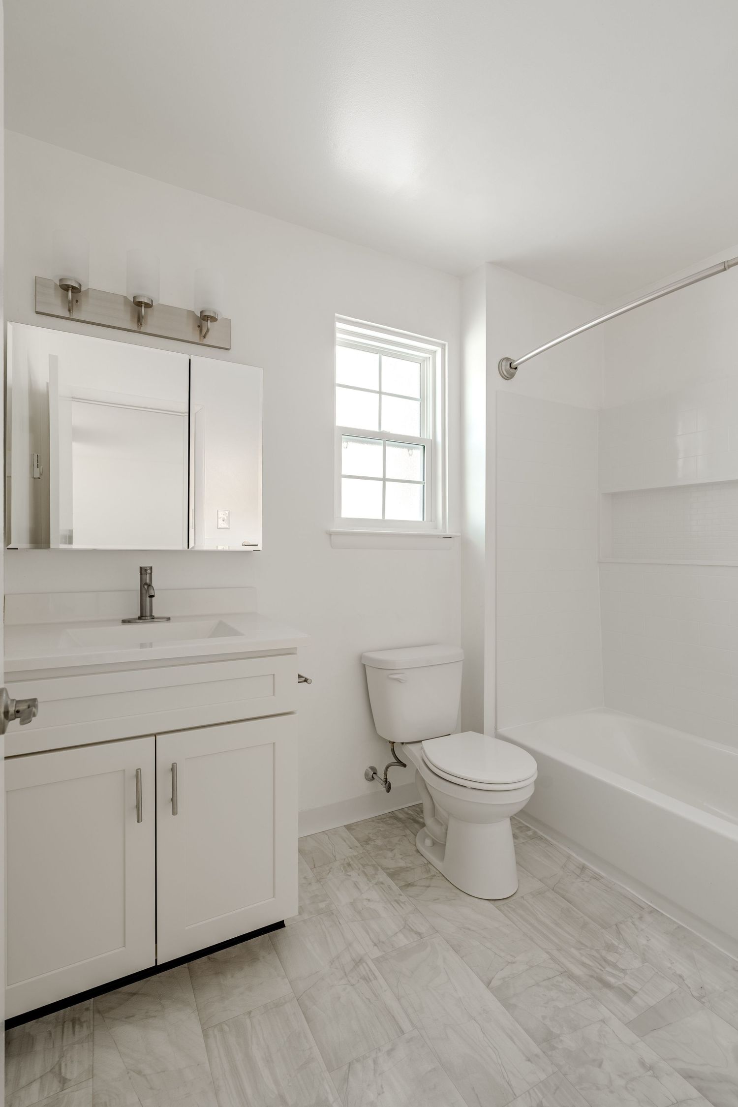 Full bathroom with a white vanity, mirrored cabinet, window and tub-shower combo