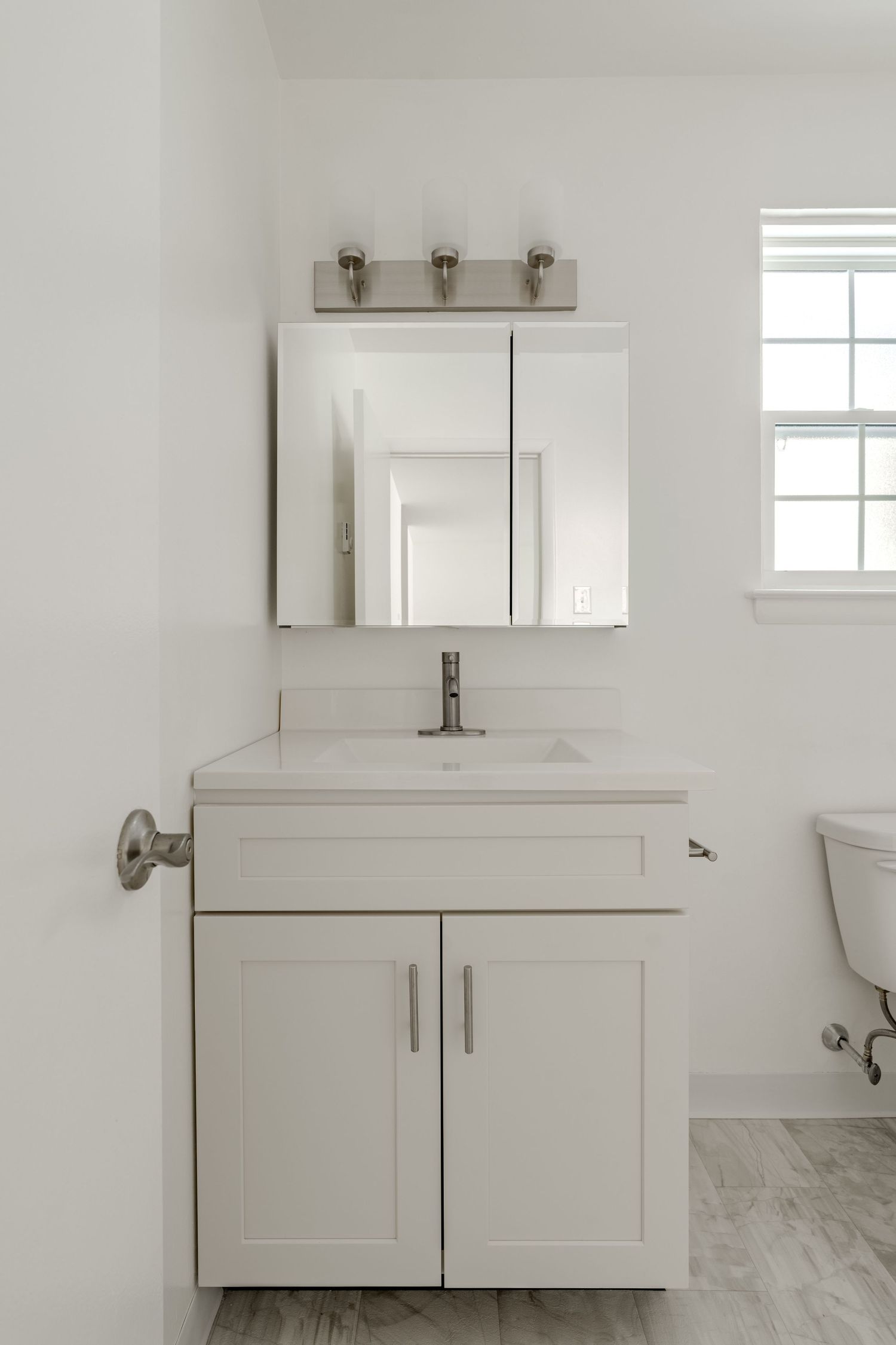 Bathroom vanity with a mirrored medicine cabinet, brushed nickel sconce and white countertop
