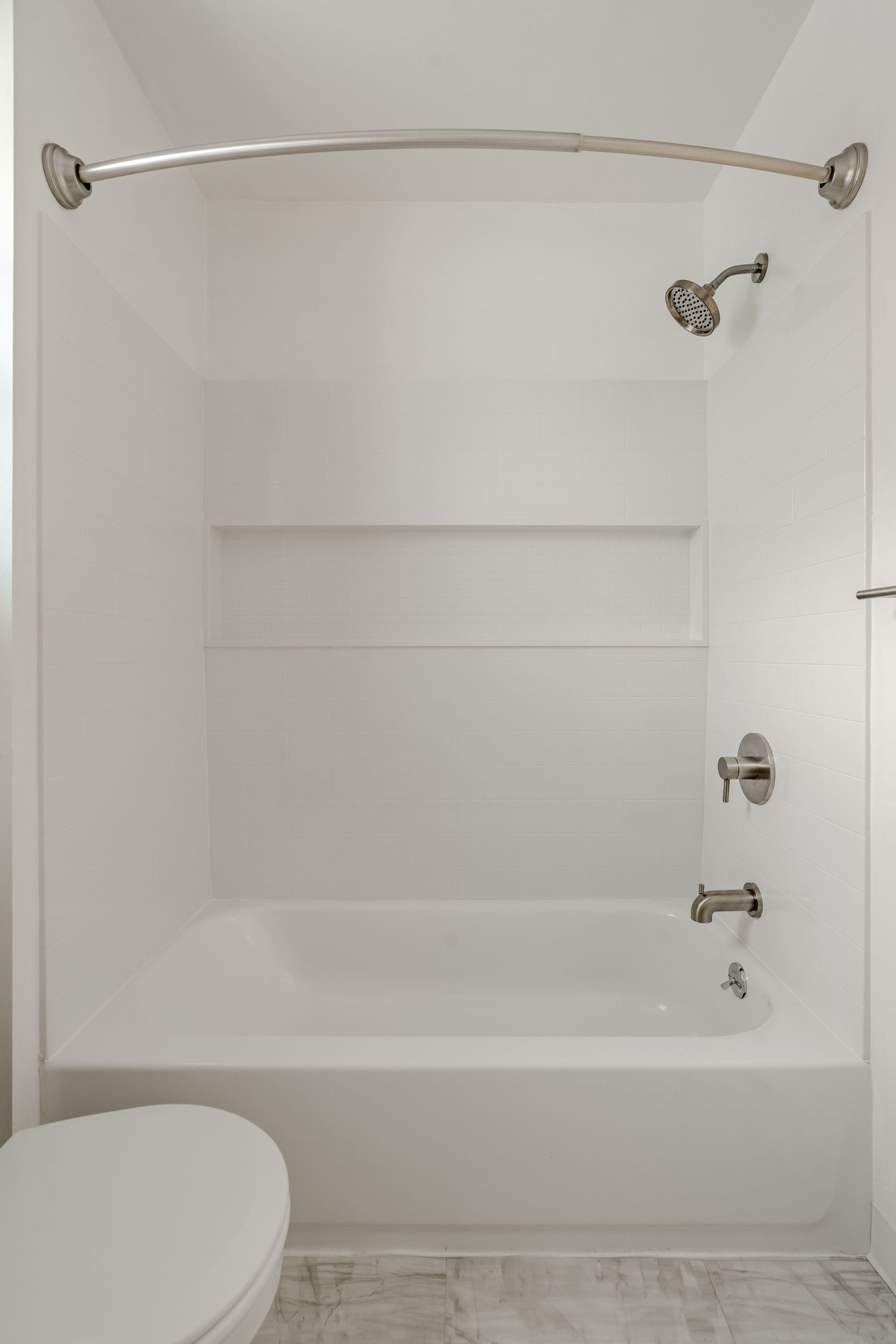 White tub-shower combo with a tiled shelf niche and curved shower rod