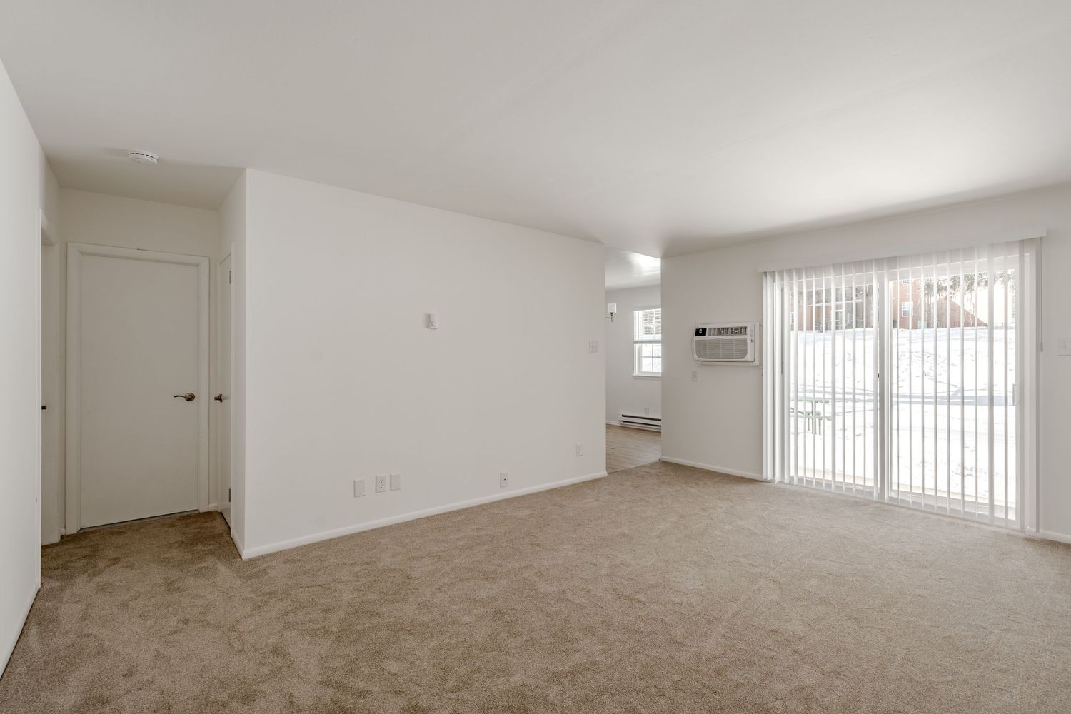 Empty carpeted living room with a sliding glass door and a wall air conditioner