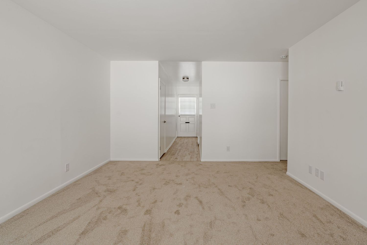 Empty carpeted room opening to a hallway with a back door and window
