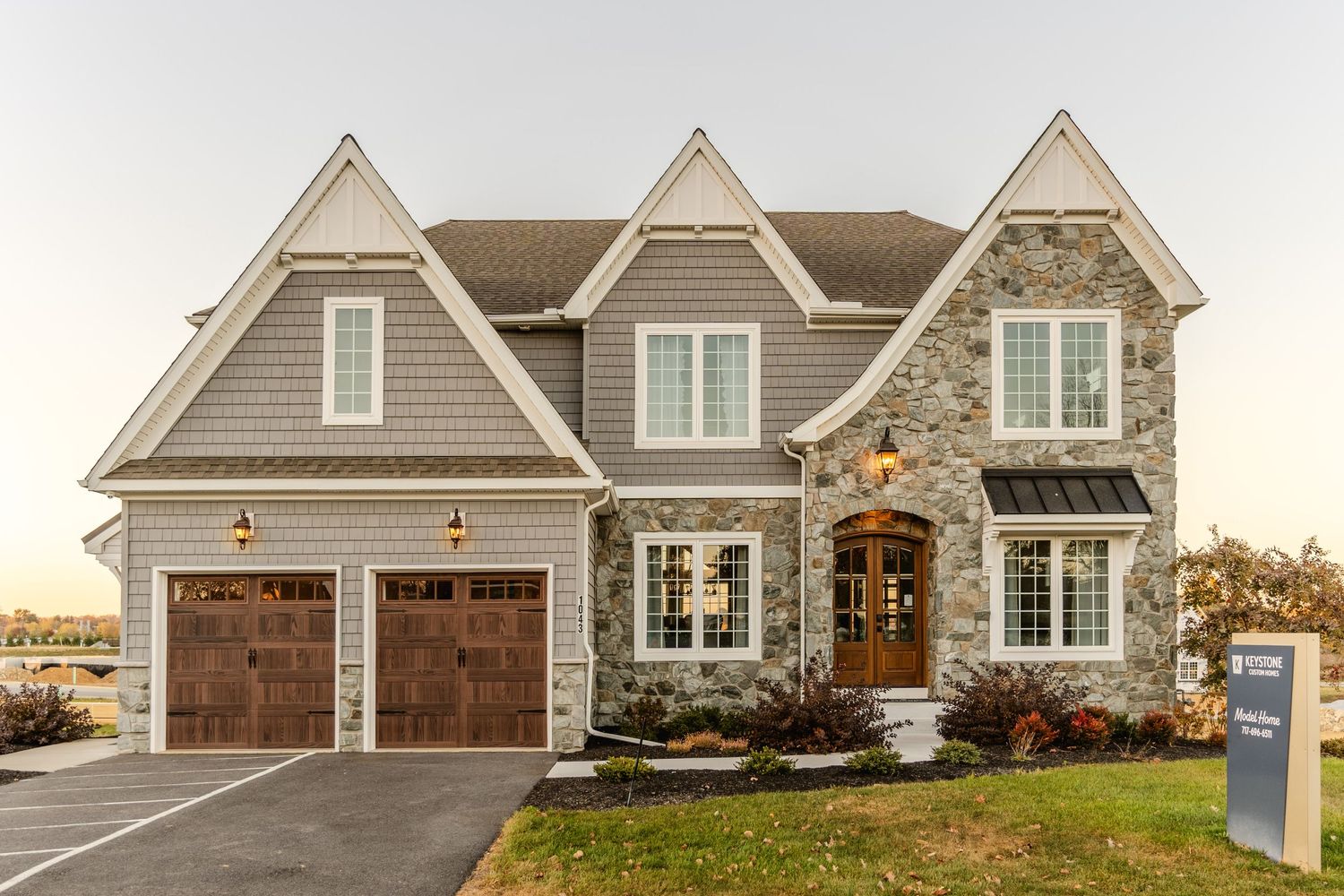 Stone and shingle two-story model home with a covered entry, dual wood garage doors and gabled roofline