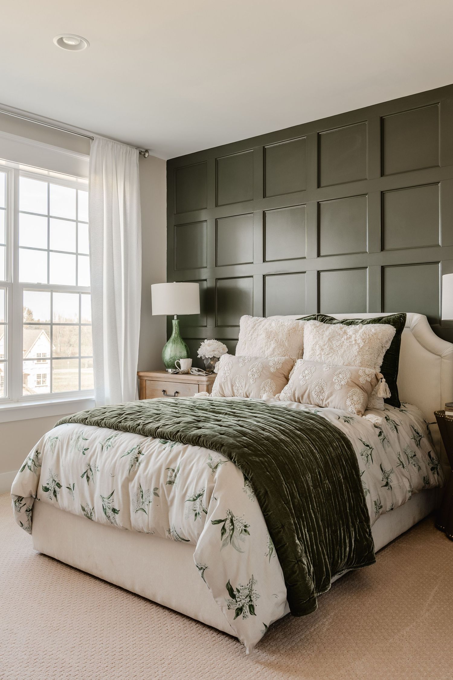 Primary bedroom with an olive paneled accent wall, upholstered headboard and green velvet throw
