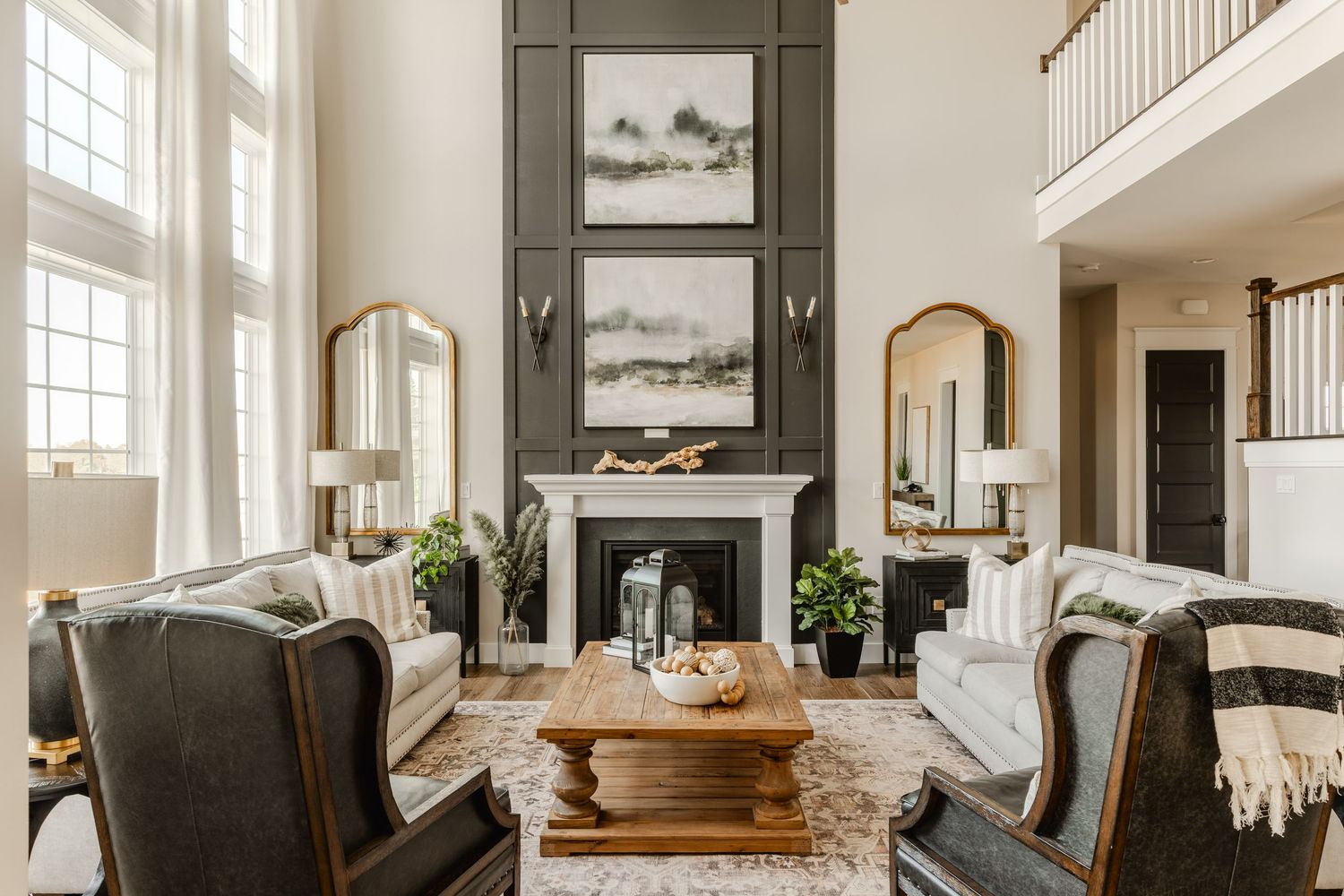 Two-story great room with dark fireplace wall, leather wingback chairs and a wood beam coffee table