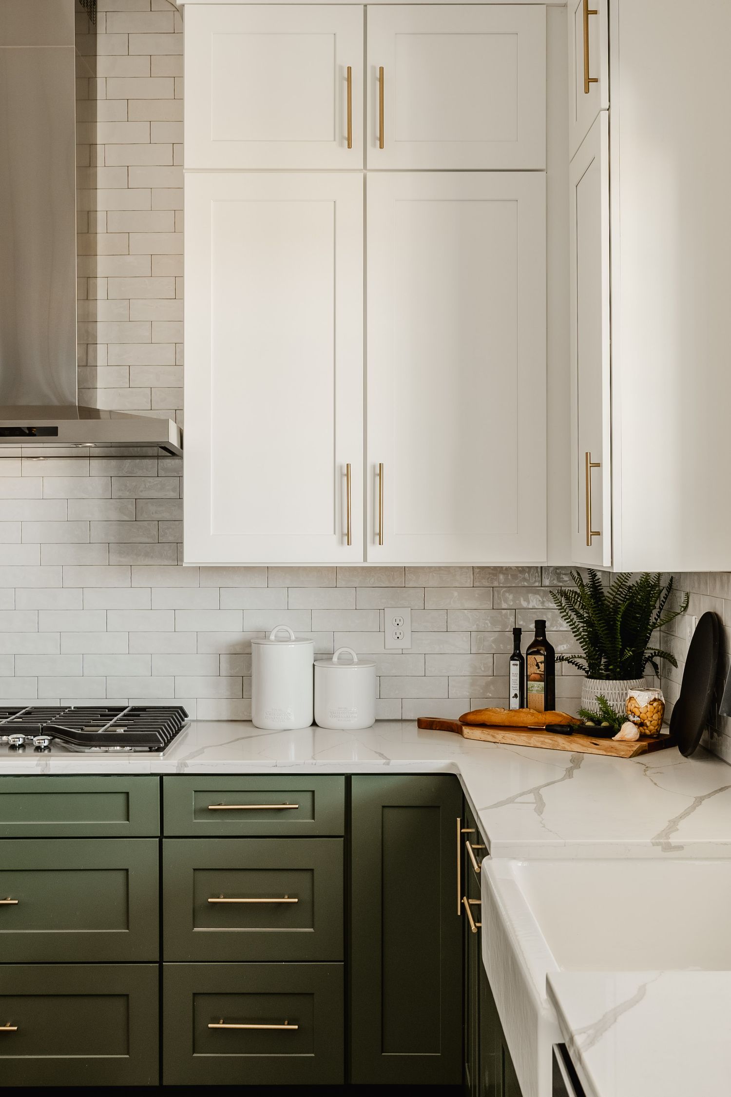 Close-up of white upper cabinetry with brass pulls above olive green lower cabinets and marble counters