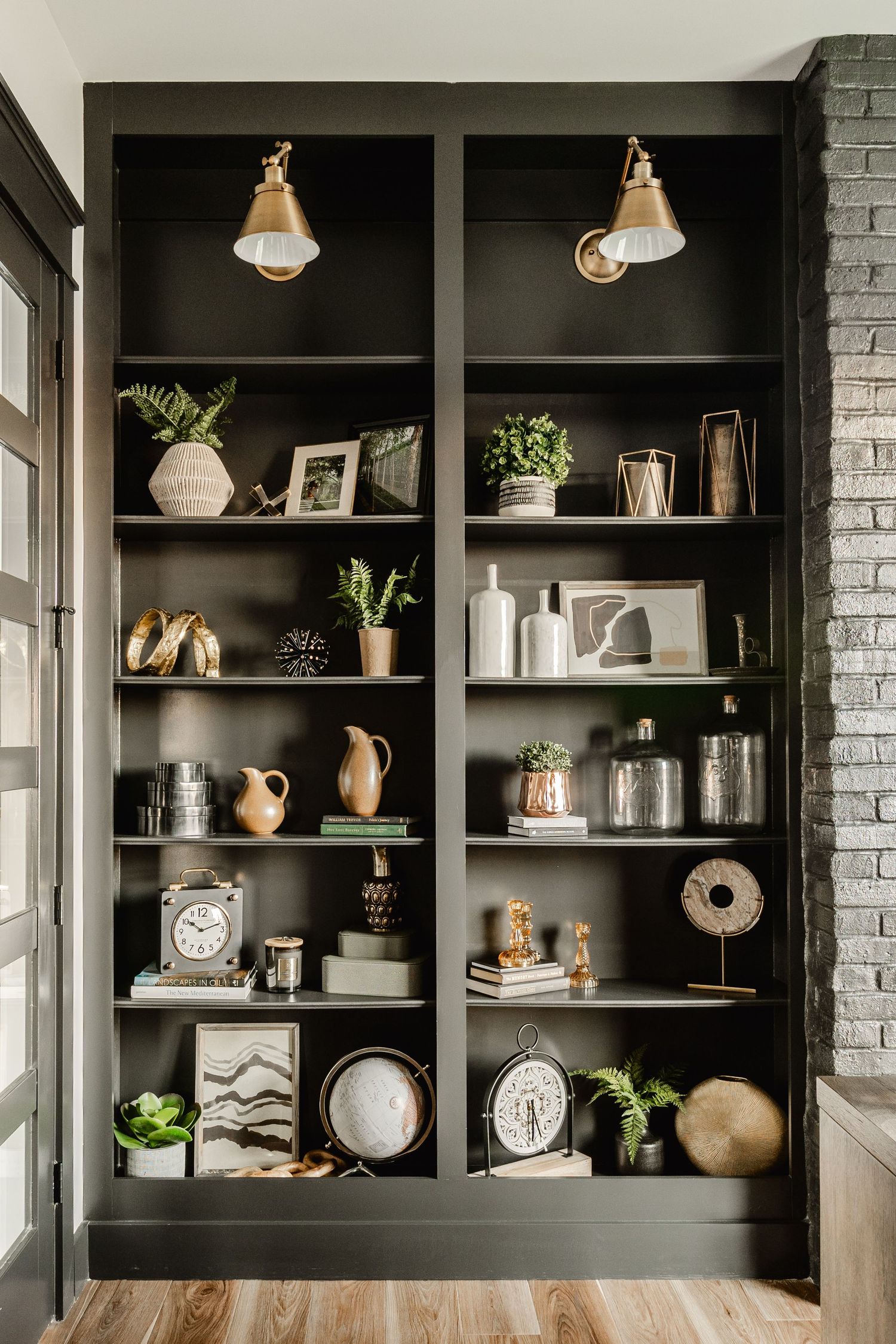 Built-in dark bookshelves styled with brass sconces, ceramics, books and a globe