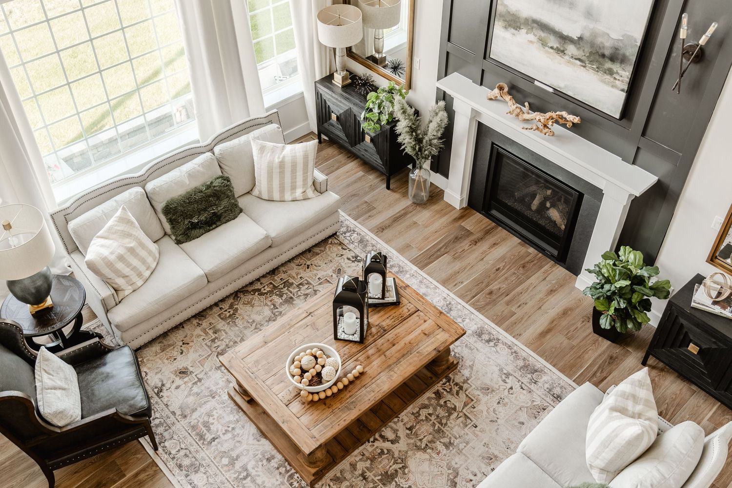 Elevated view of an open living room with cream sofas, patterned rug and a dark fireplace wall