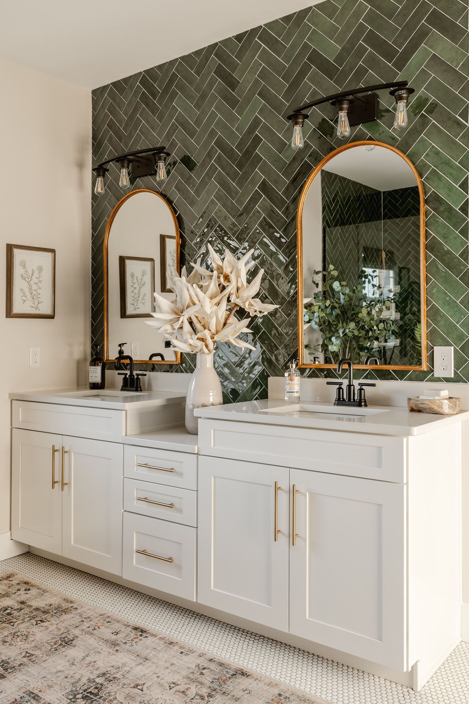 Double vanity with green herringbone tile, arched brass mirrors and black sconce lighting