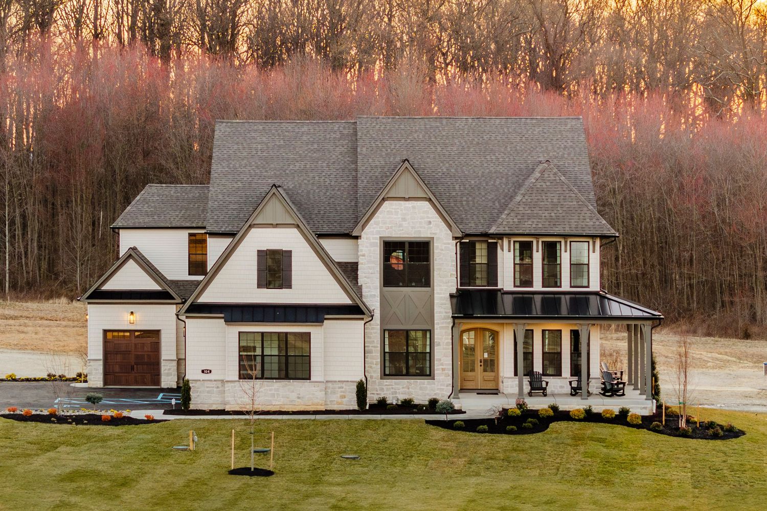 Cream and stone two-story home with a covered wraparound porch glowing at sunset