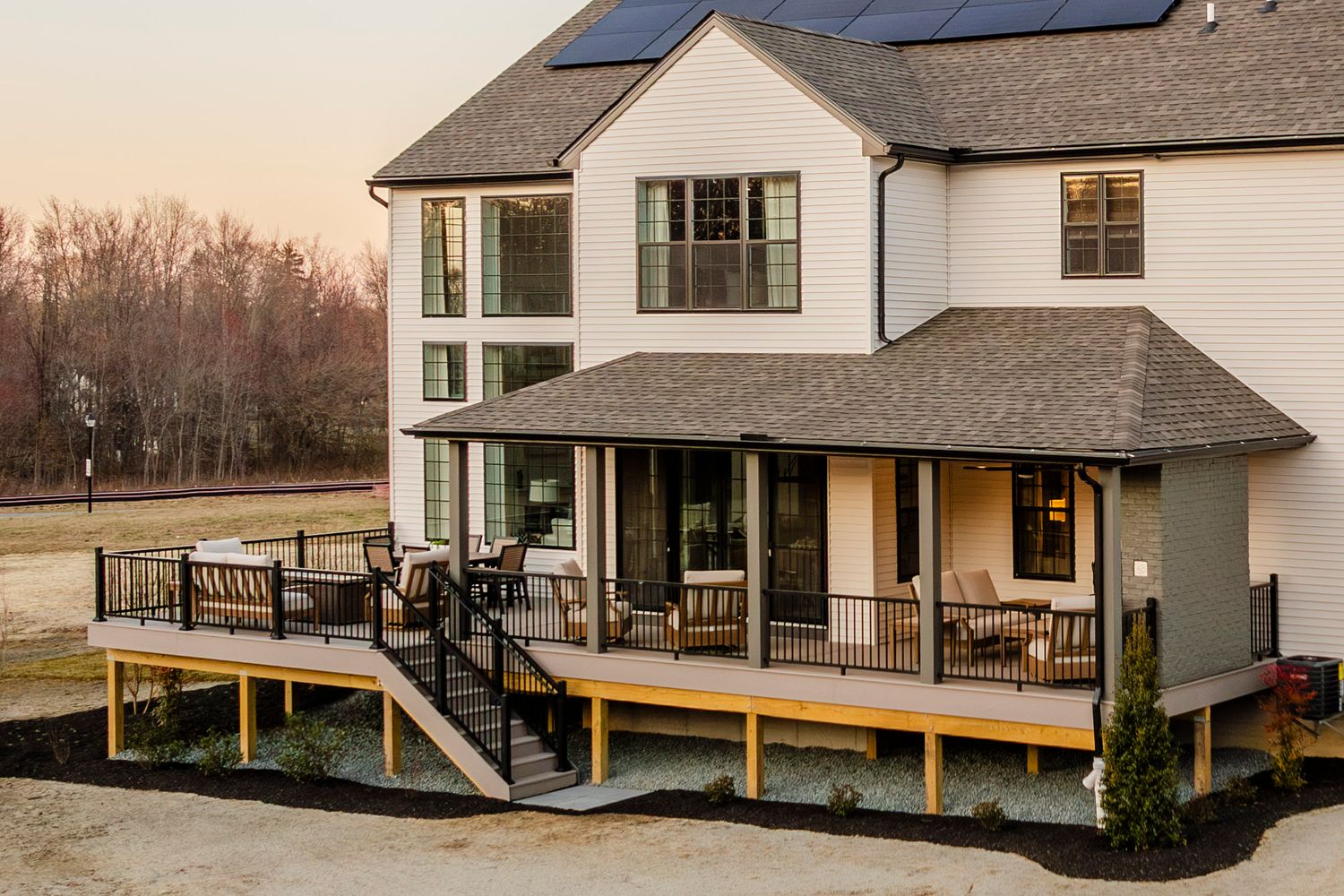 Aerial rear view of a white home with solar panels, a covered deck and outdoor seating