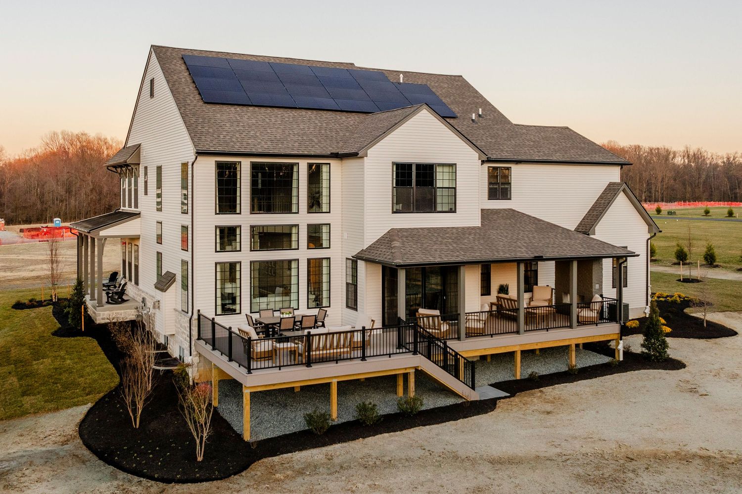 Aerial view of a large white home's rear elevation with solar roof and wraparound covered deck