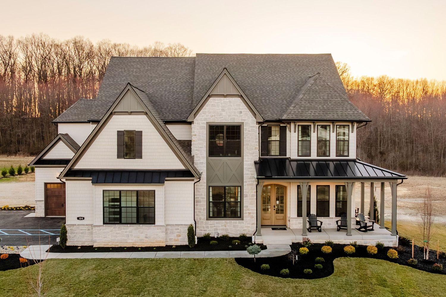 Tudor-style stone and shingle home with steep gables, a covered porch and rocking chairs at sunset