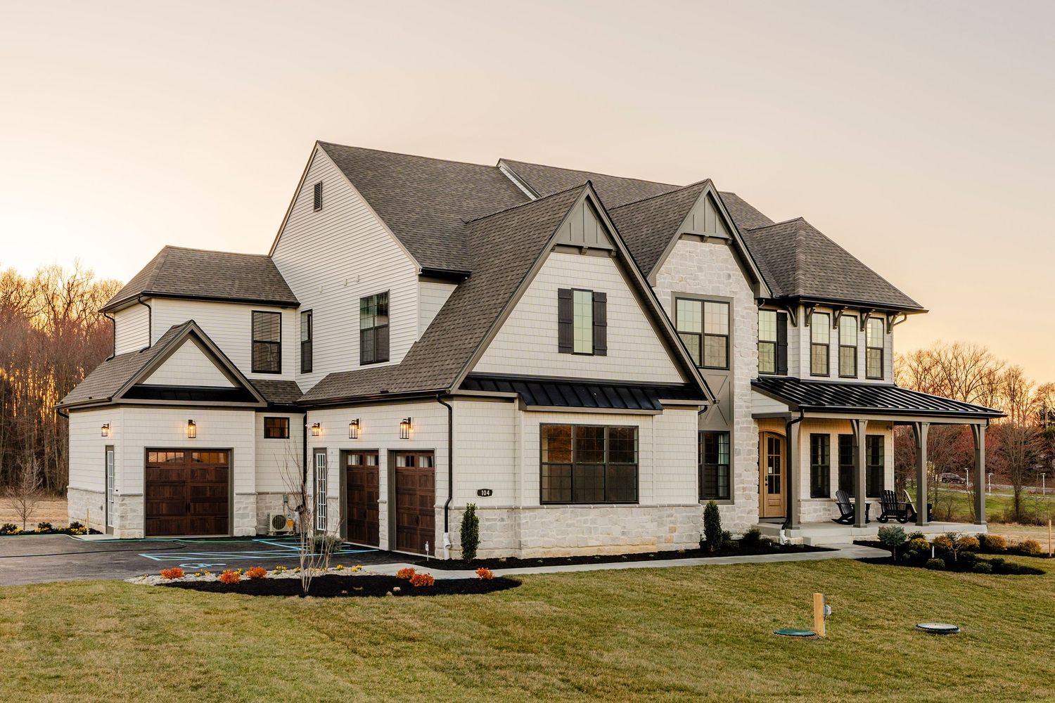 Front elevation of a large cream shingle-style home with a stone base and three wood garage doors