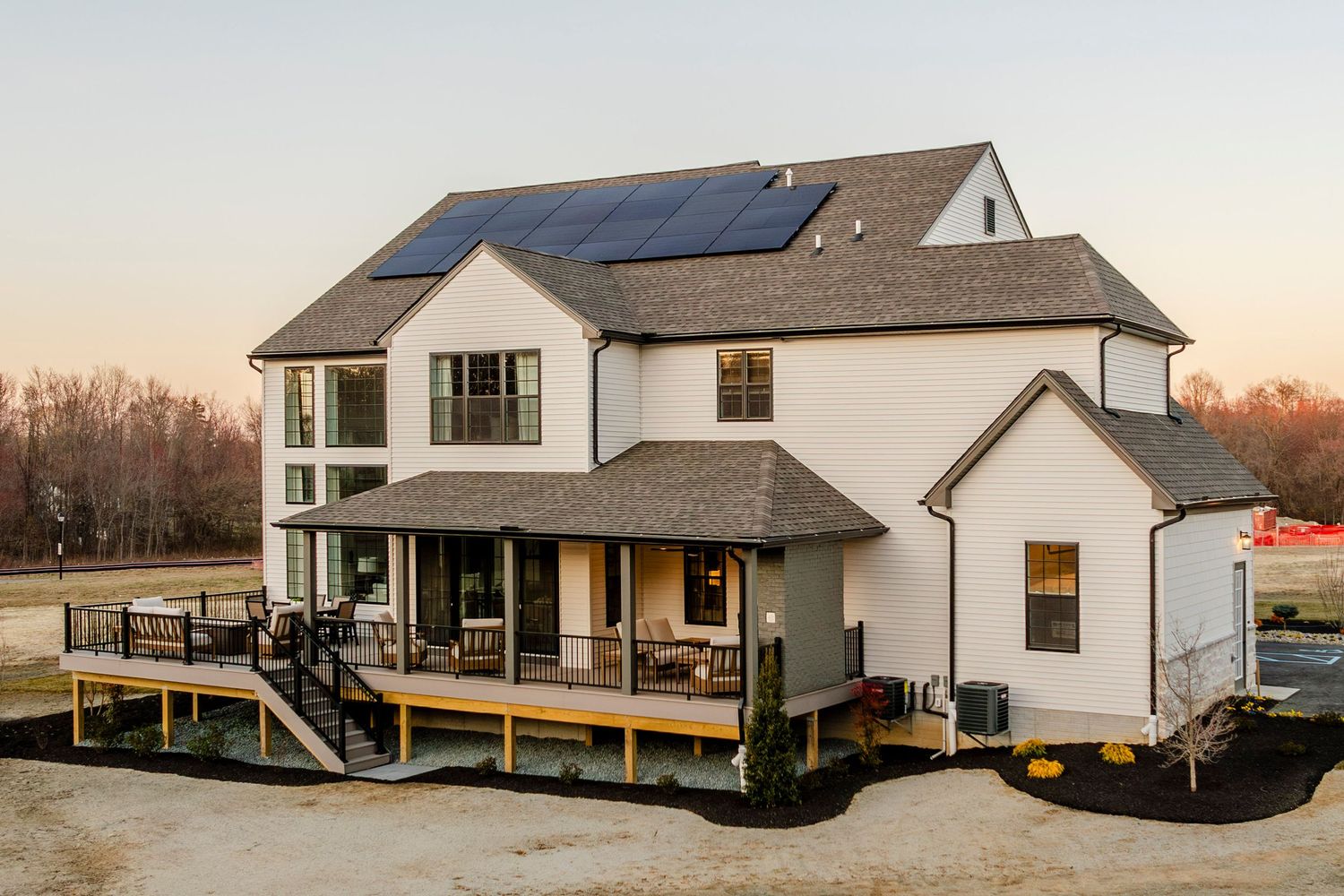 Rear exterior of a white farmhouse with rooftop solar panels and a covered back porch