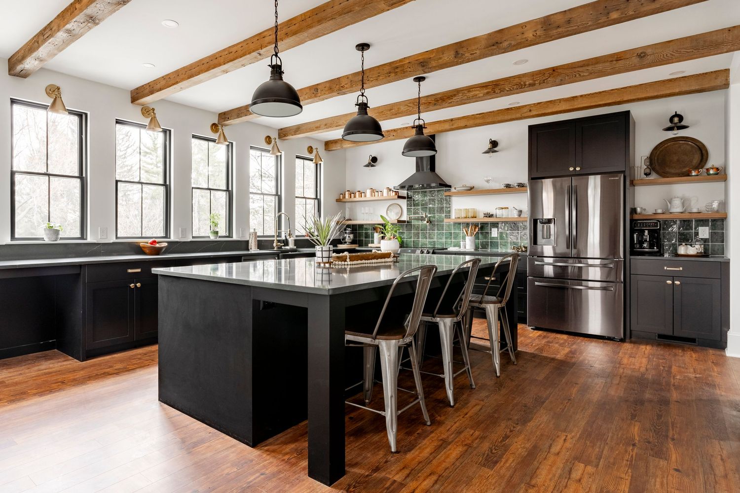 Kitchen with a black island, gray countertop, metal stools and a stainless refrigerator