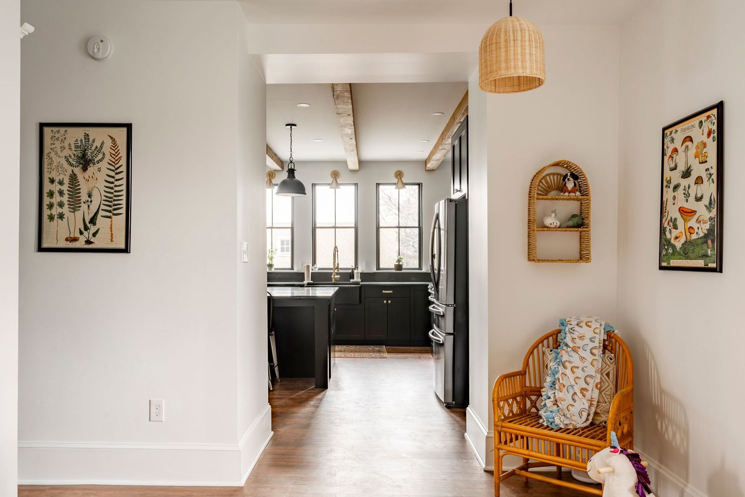 Mudroom hallway with black doors, wood floors and a view into the kitchen beyond