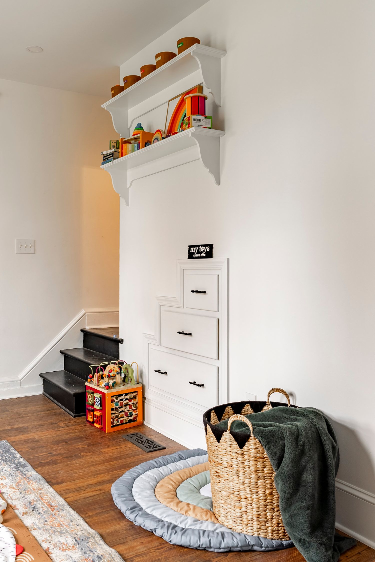 Playroom nook with black built-in stair storage drawers, a play mat and toy baskets