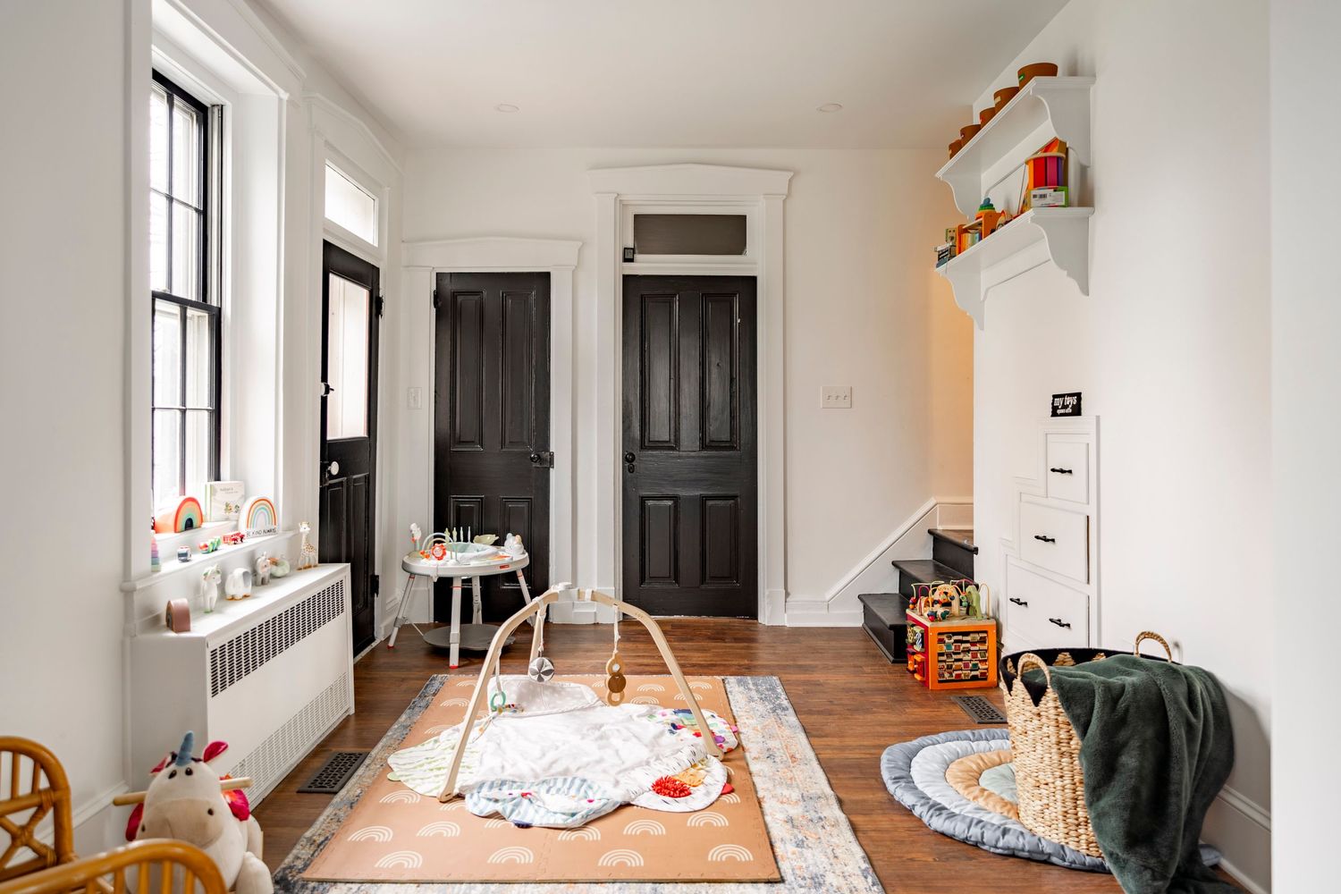Kids playroom with black paneled doors, a play mat and built-in staircase storage