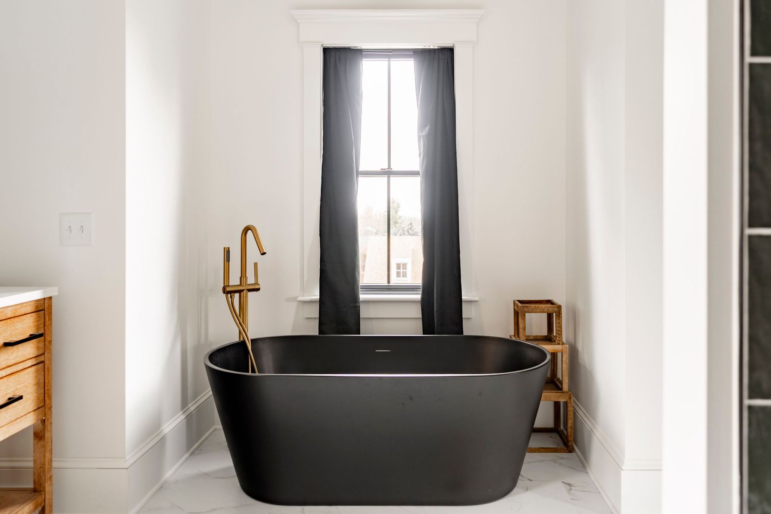 Close-up of a black soaking tub with a gold floor-mount faucet beneath a curtained window