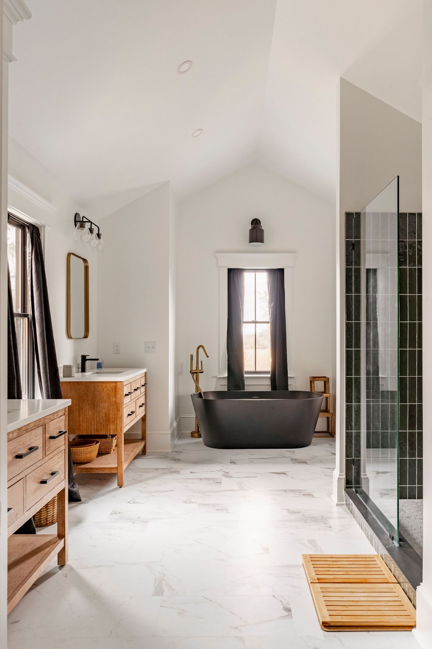 Primary bathroom with a black freestanding tub, marble floor and wood vanities
