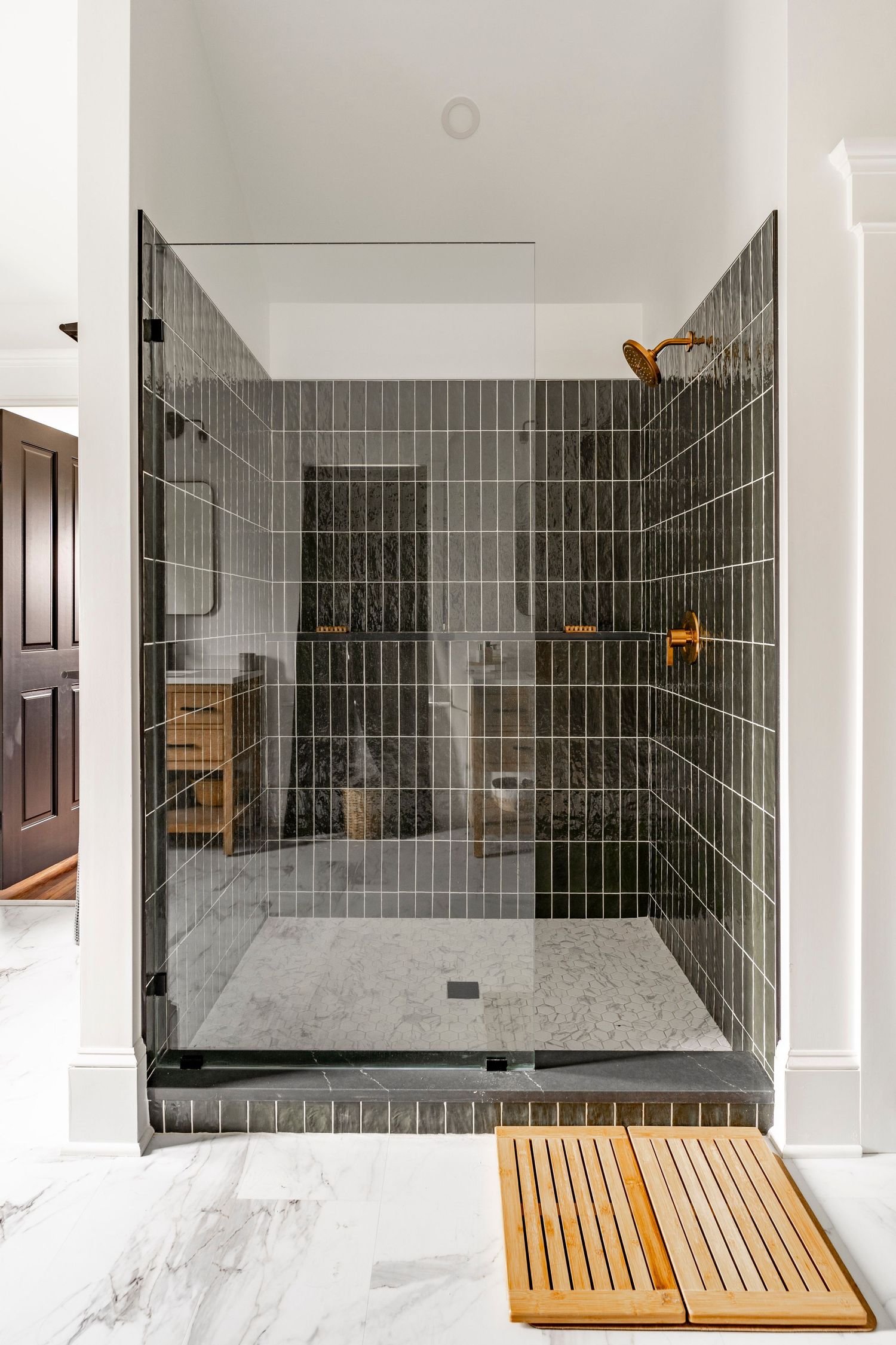 Glass-enclosed shower with dark vertical subway tile and brass fixtures