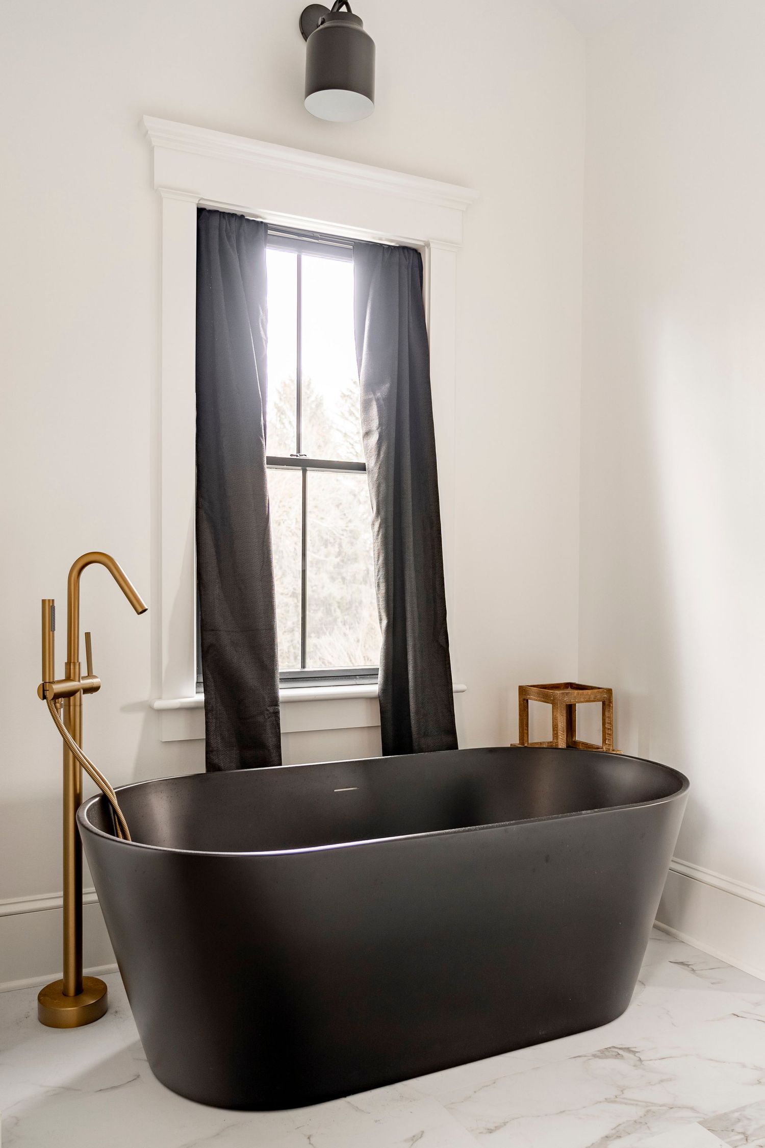 Close-up of a black soaking tub with a gold floor-mount faucet
