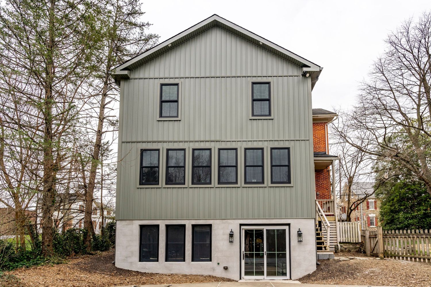 Exterior of a three-story home with sage green board-and-batten siding and black windows