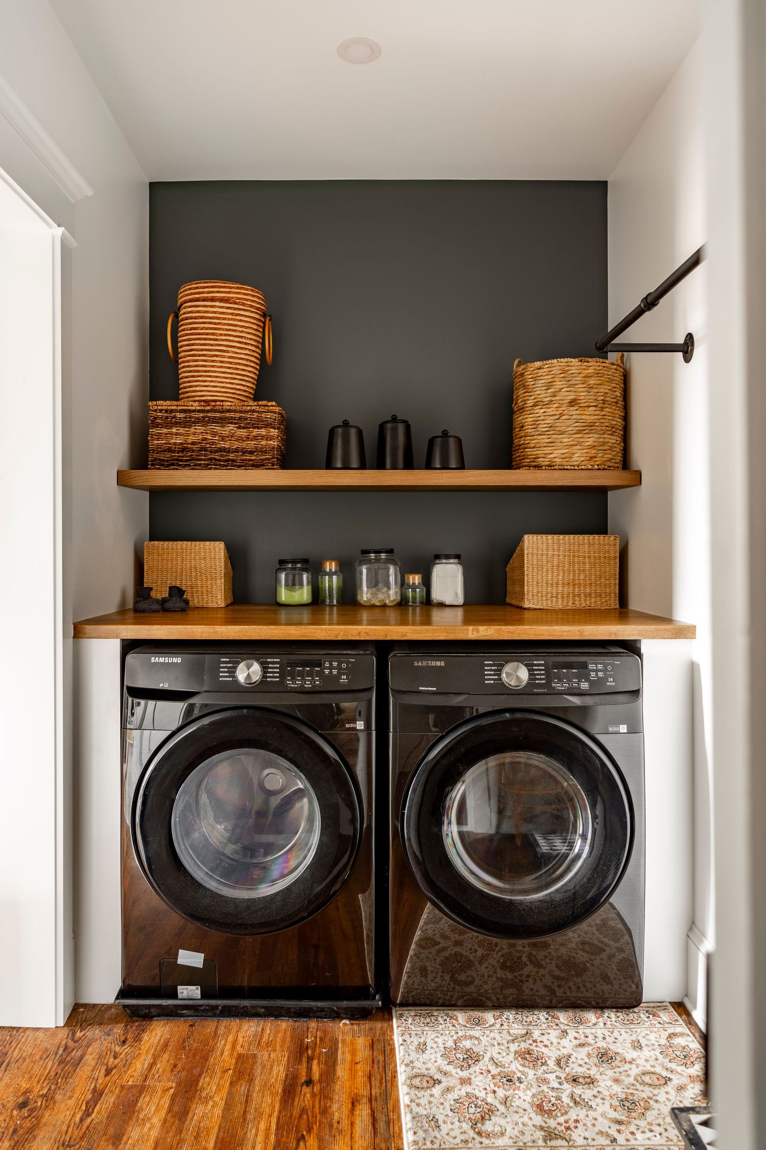 Laundry room with a black front-load washer and dryer beneath a wood shelf with baskets