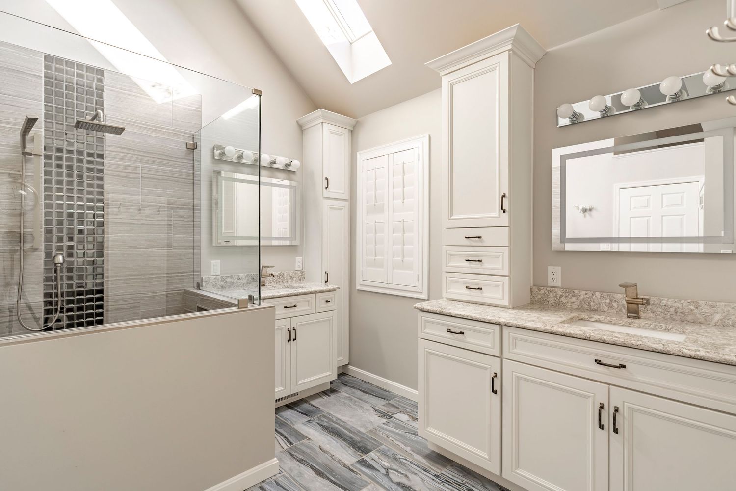 Primary bathroom with dual vanities and a skylight over the glass-enclosed shower