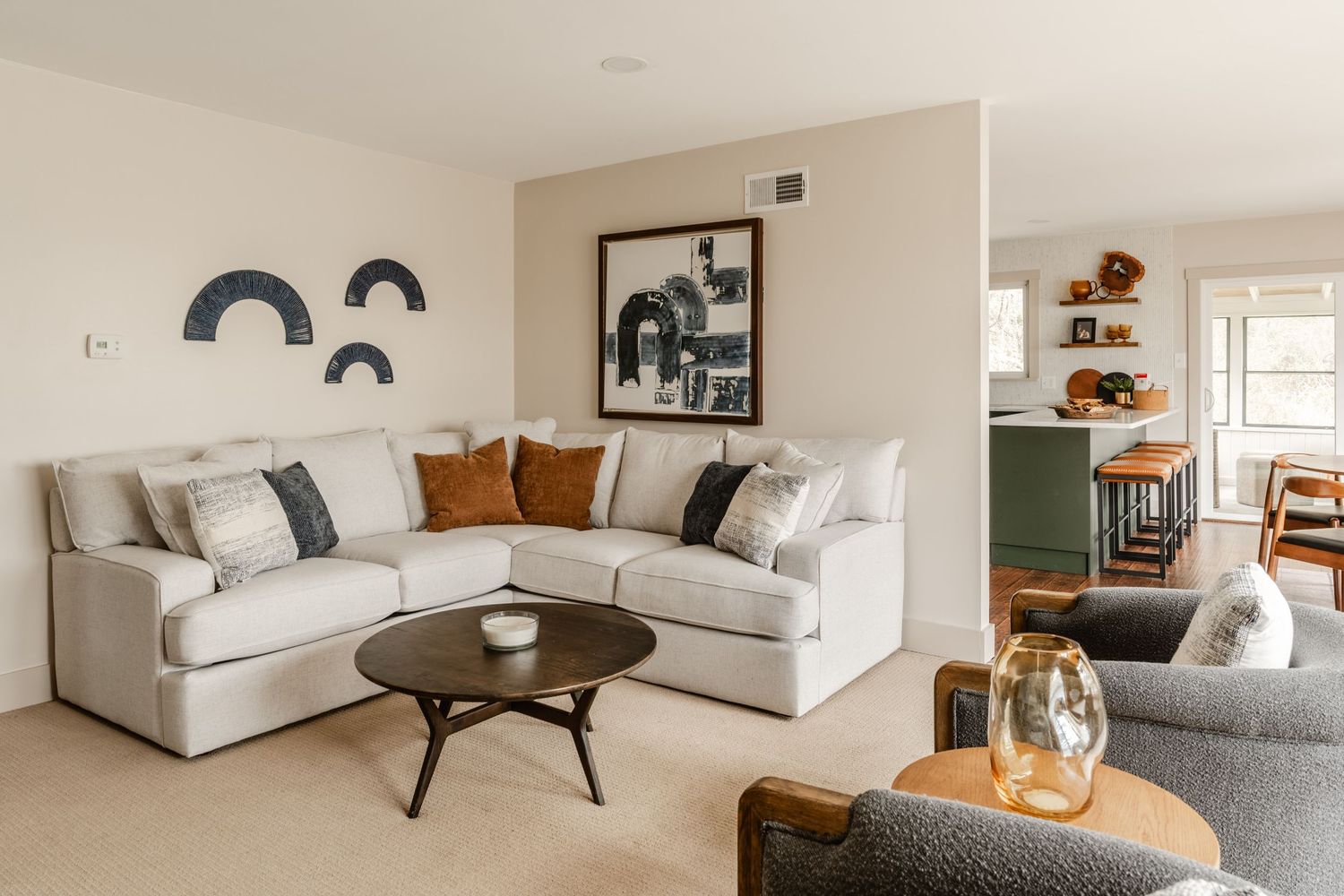Living room with a cream sectional sofa, ceramic wall art and a view into the open kitchen