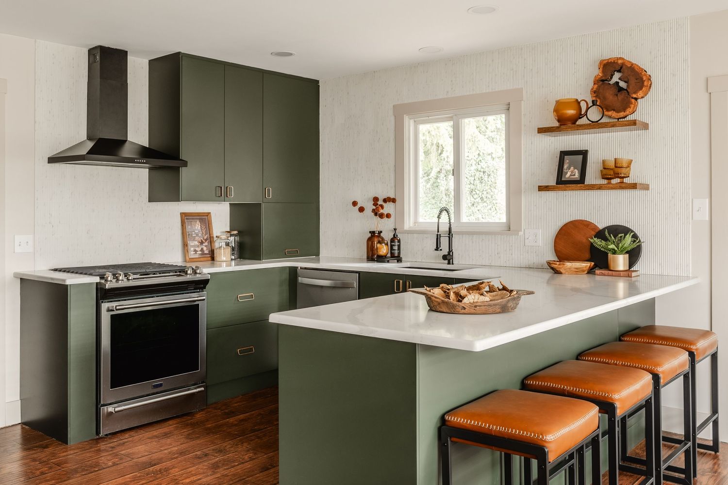 Kitchen with a black vented range hood, olive cabinetry and floating shelves above a marble counter