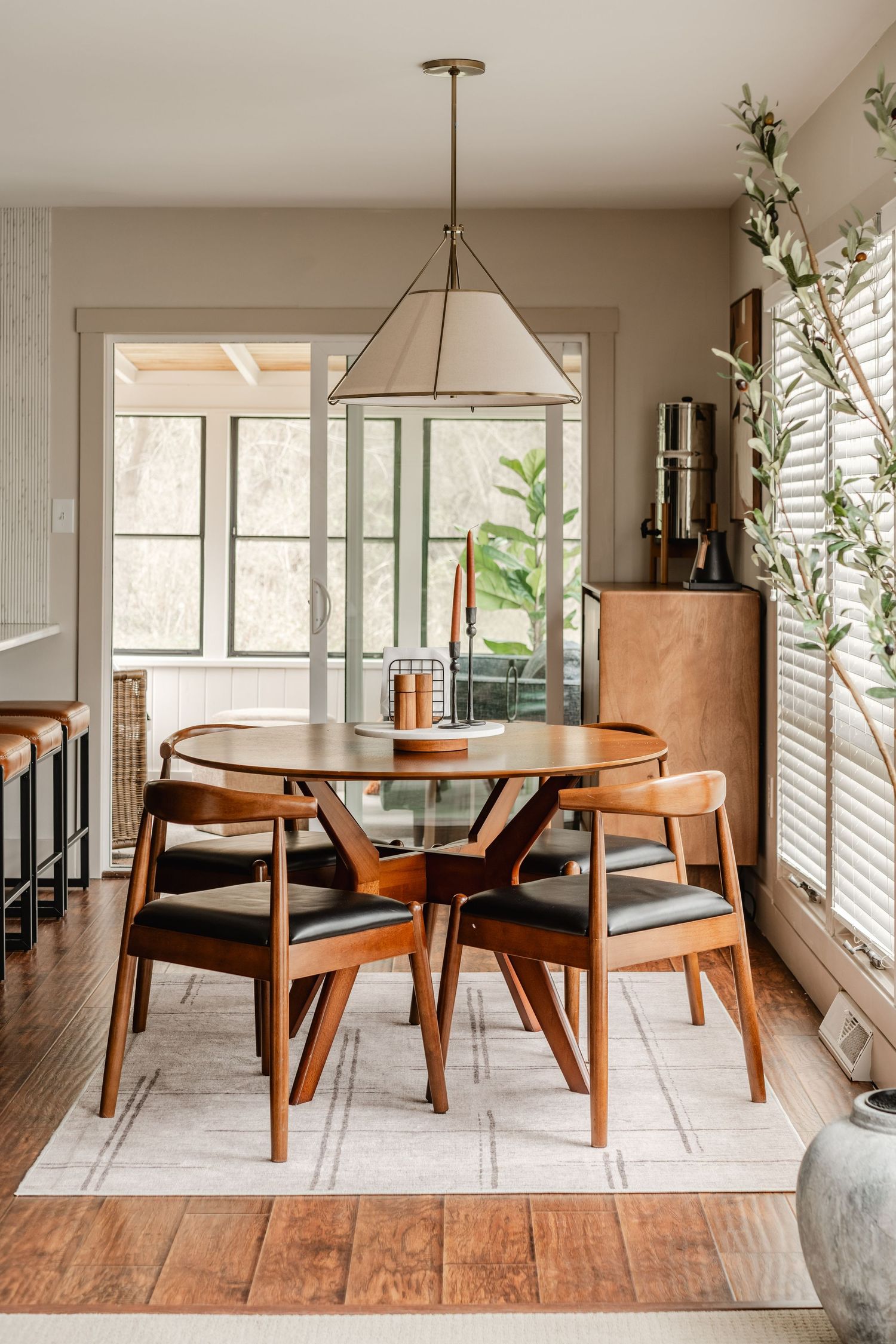 Dining nook with a round wood table, black leather chairs and a linen drum pendant light