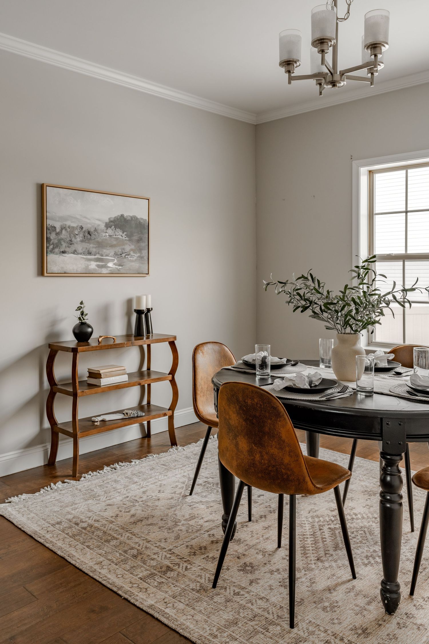Dining room with a round black table, cognac leather chairs and a three-tiered wood console