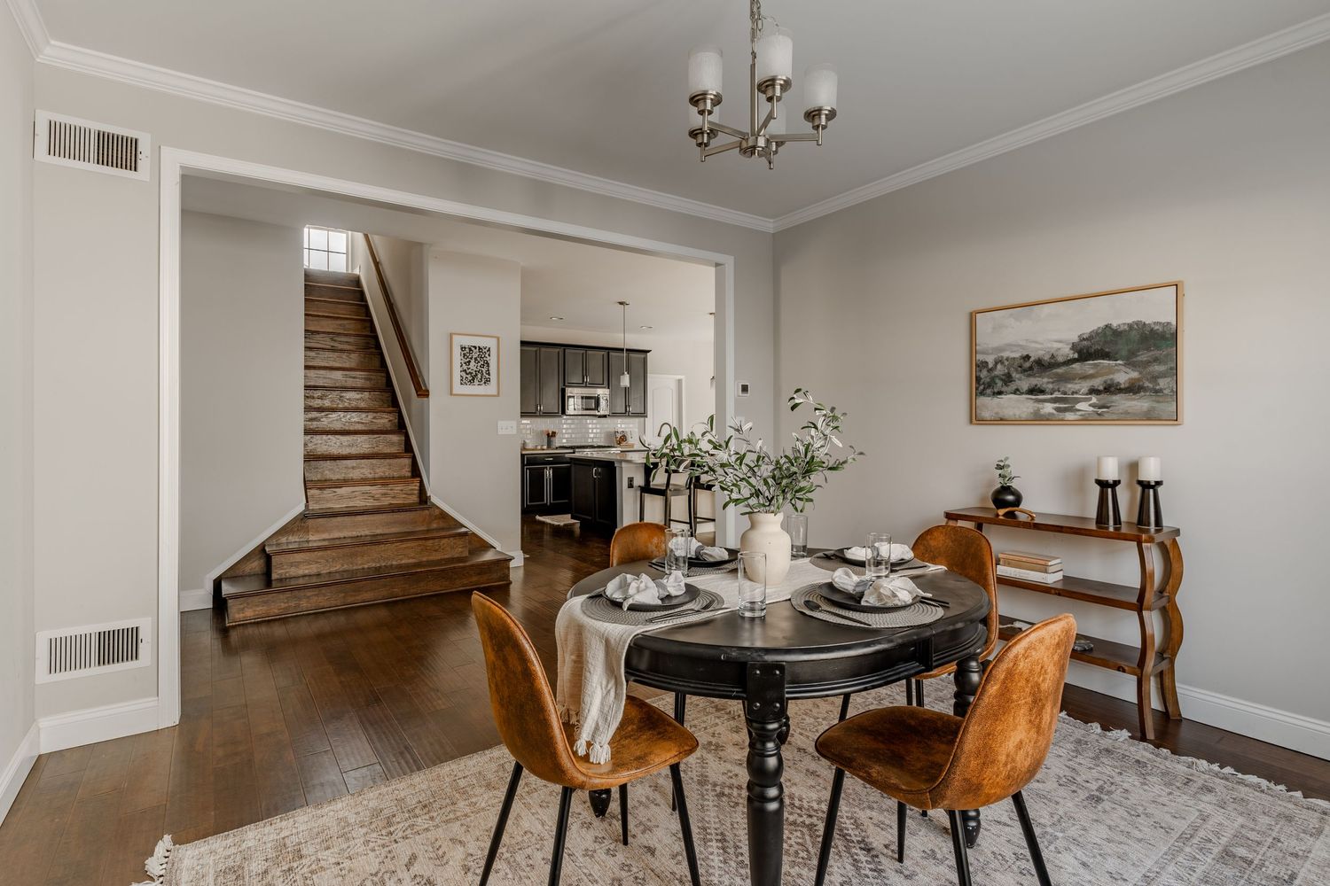Dining room with a round black table and leather chairs opening to a wood staircase and kitchen