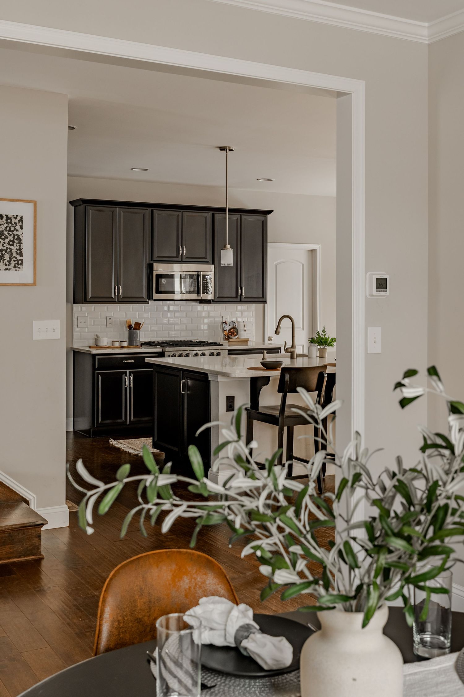 View into a dark cabinetry kitchen with white subway tile backsplash from an olive-tree-framed doorway