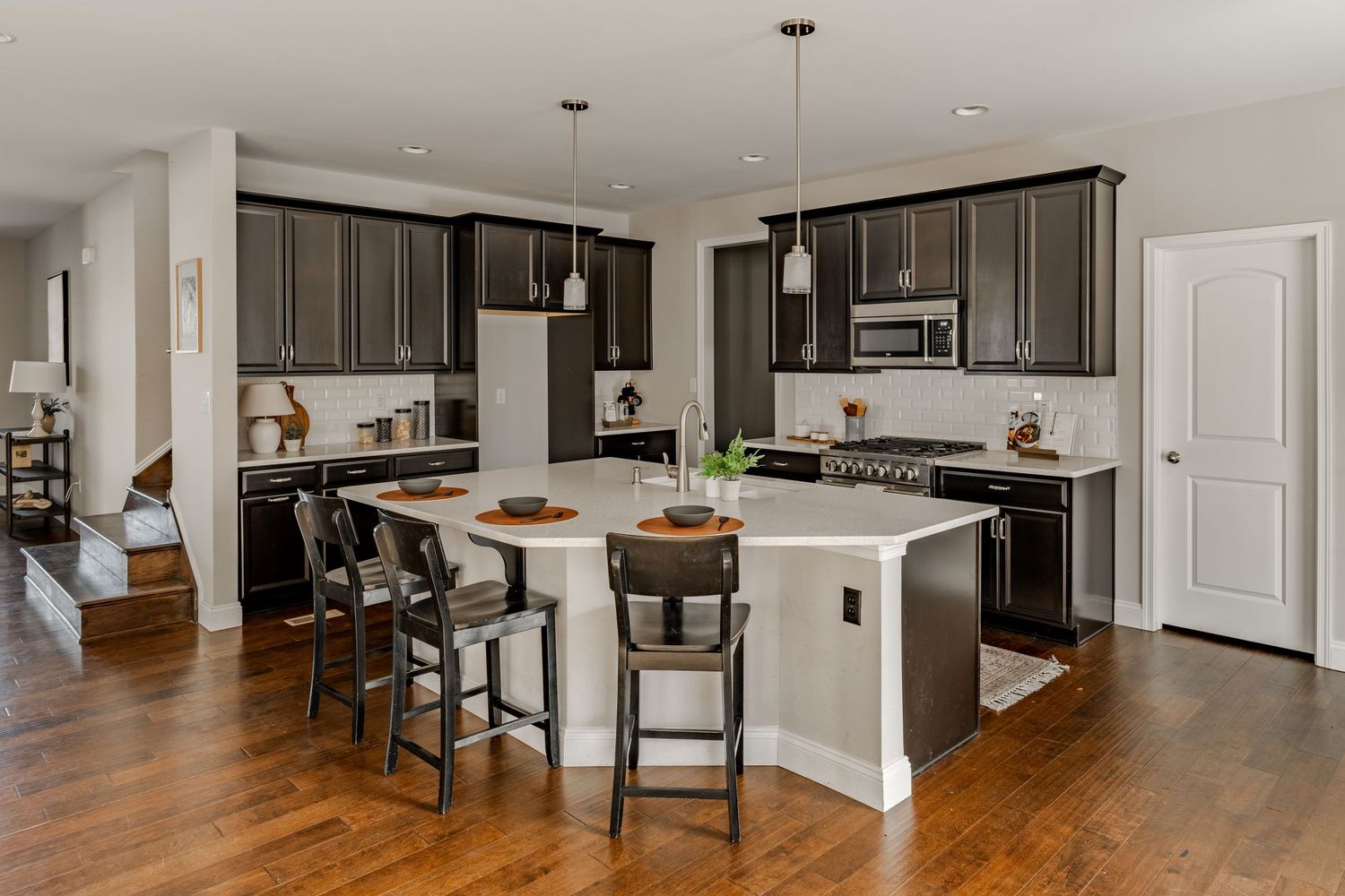 Kitchen with dark cabinetry, white subway tile backsplash and an island seating three at the counter