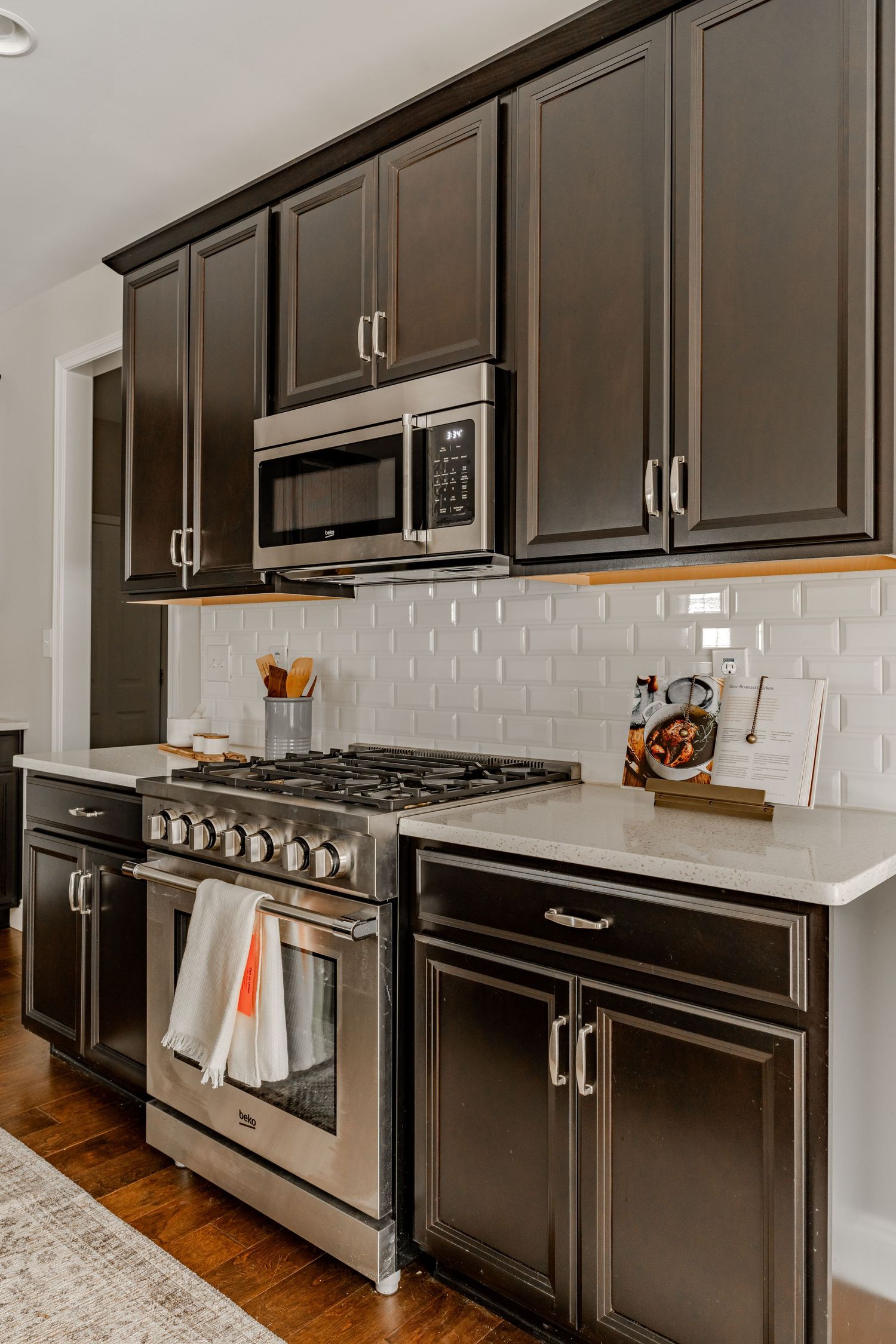 Close-up of a stainless gas range and subway tile backsplash between dark kitchen cabinets