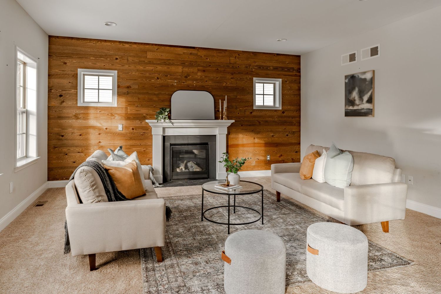 Living room with a wood plank accent wall, white fireplace and cream sofas with mustard pillows