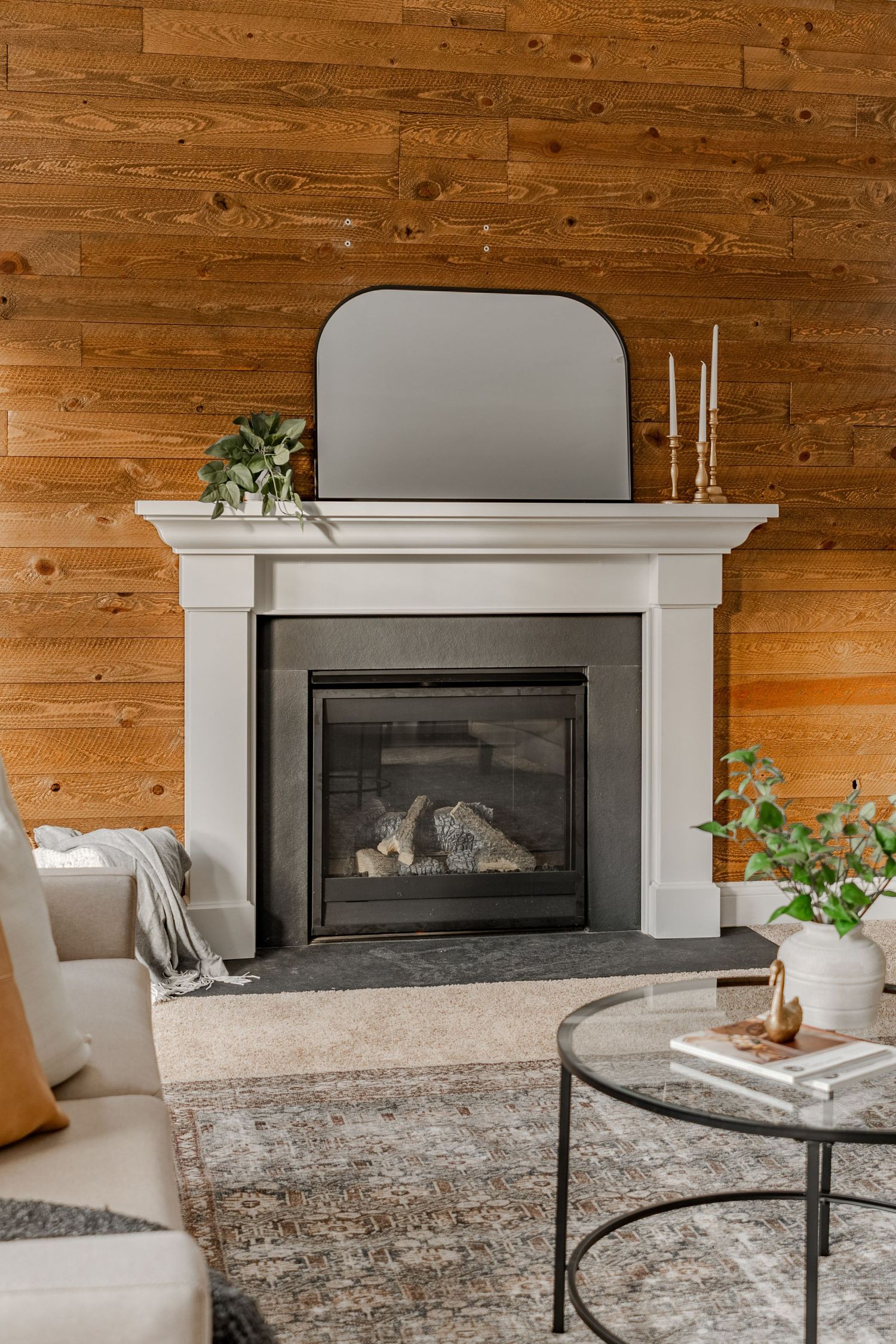 Close-up of a white fireplace mantel with an arched mirror and brass candlesticks against a wood wall