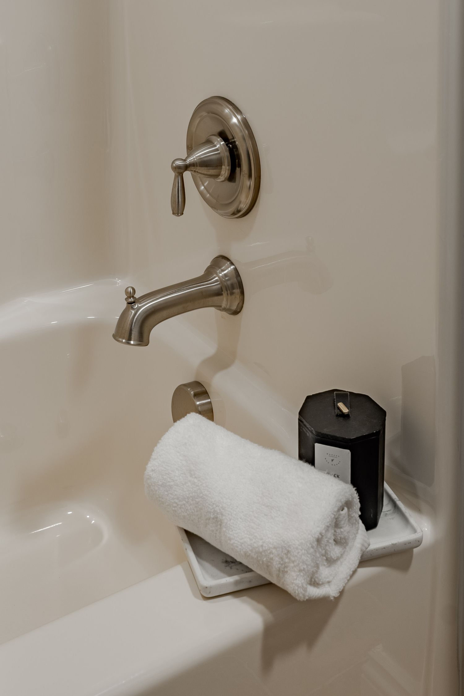 Close-up of brushed nickel tub fixtures with a rolled towel and black candle on the ledge