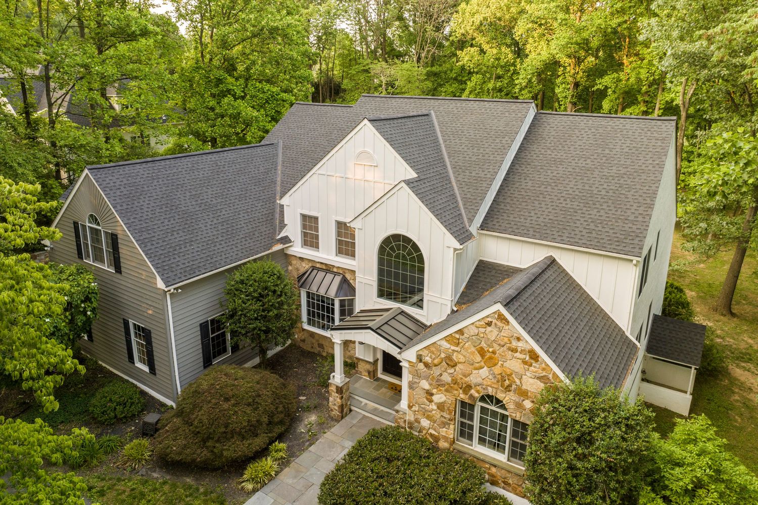 Aerial view of a multi-gabled shingle-style home surrounded by mature trees