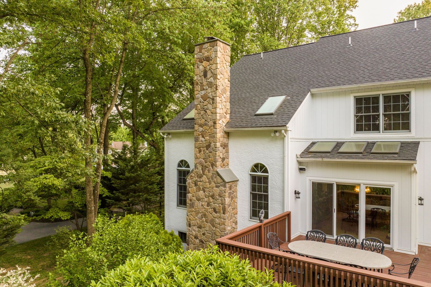 Aerial close-up of a stone chimney and arched windows above a wood deck with dining furniture