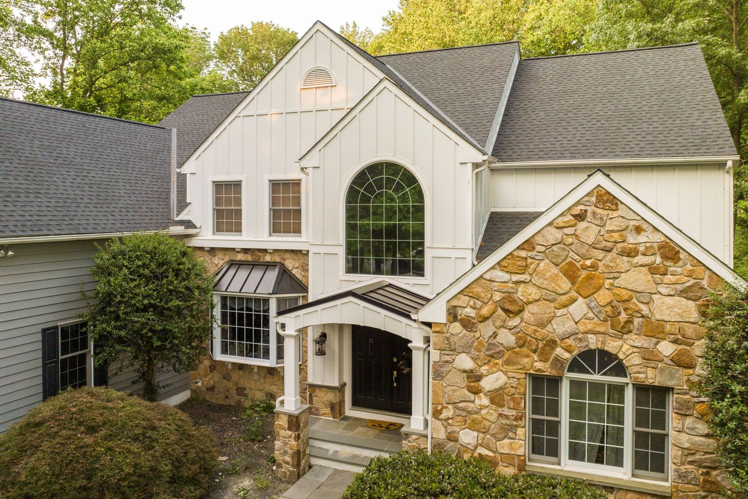 Close-up exterior of a white board-and-batten home with an arched window and stone entry surround
