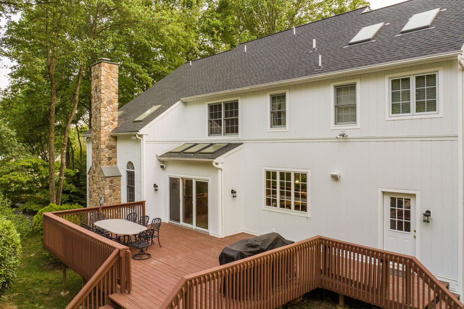 Aerial view of a wood deck with an outdoor dining set beside a tall stone chimney and sliding doors